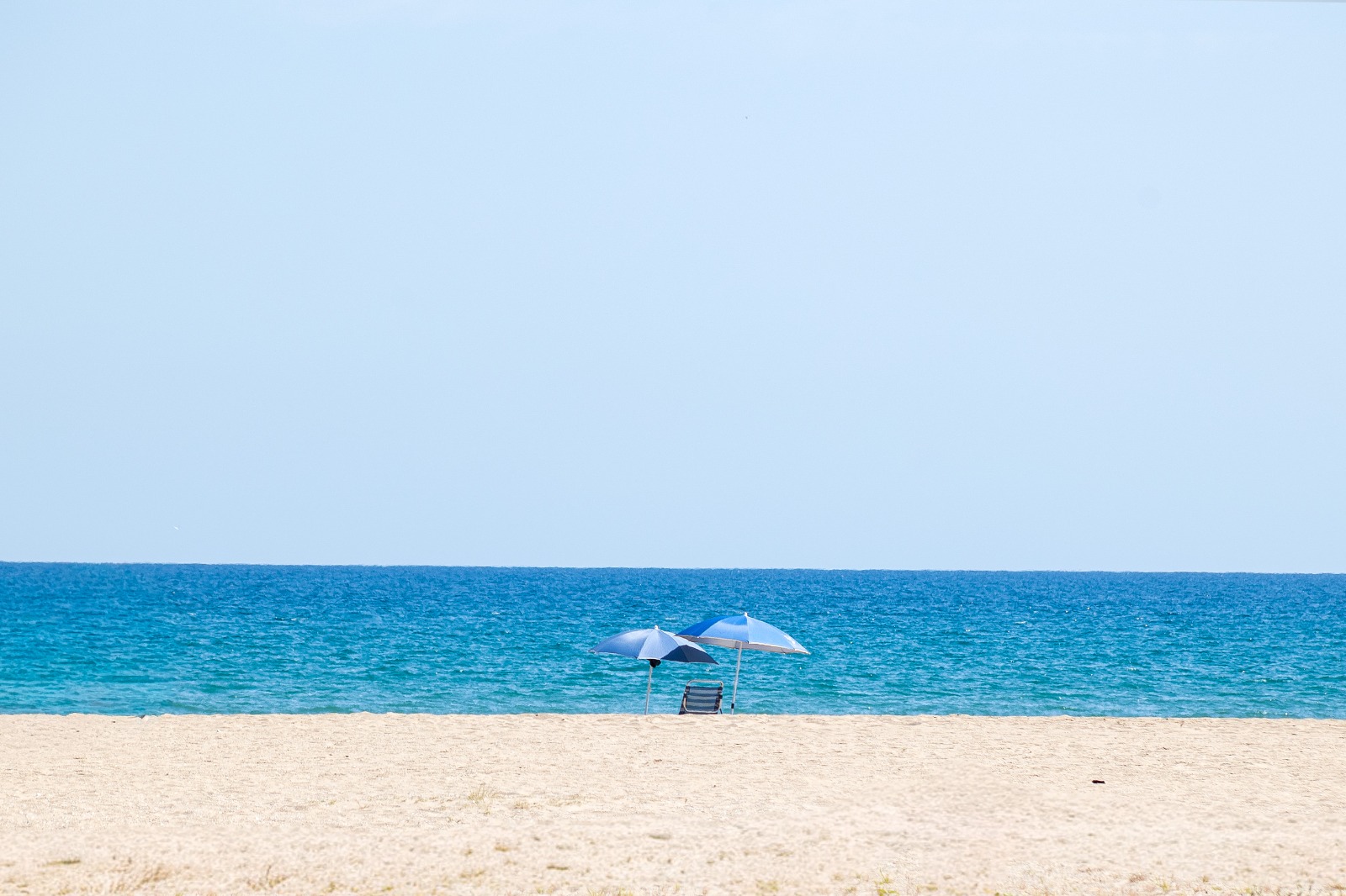 Leerer Strand mit blauen Sonnenschirmen